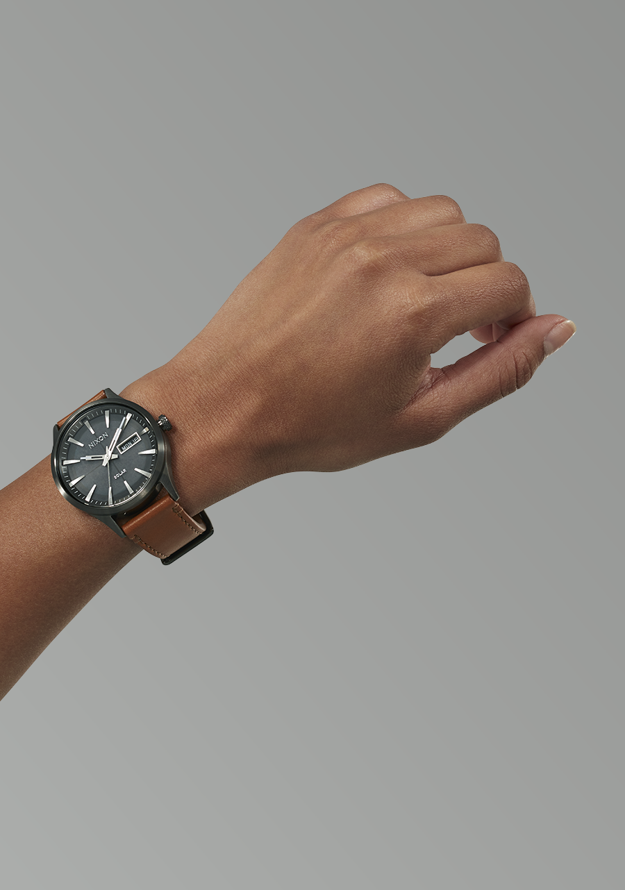 Wristwatch with a dark face and brown leather strap worn on a person’s wrist.