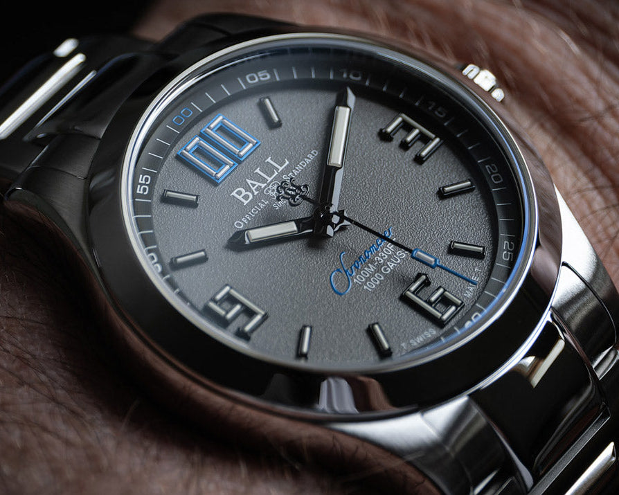 Close-up of a luxury watch with a dark face and silver band on a wooden surface.