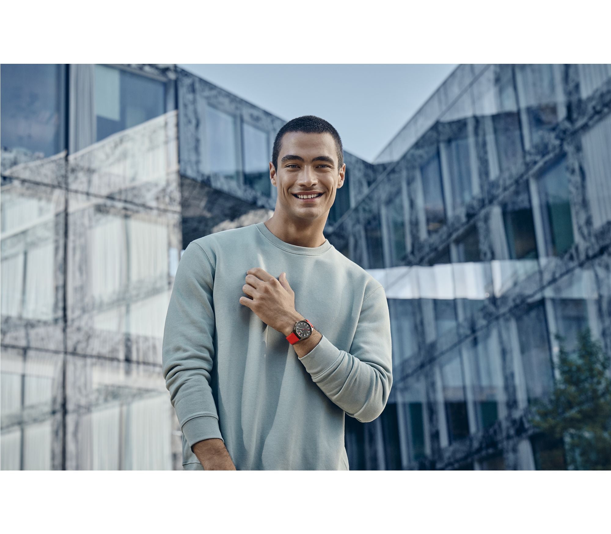 Smiling man wearing a light gray sweater and wristwatch.