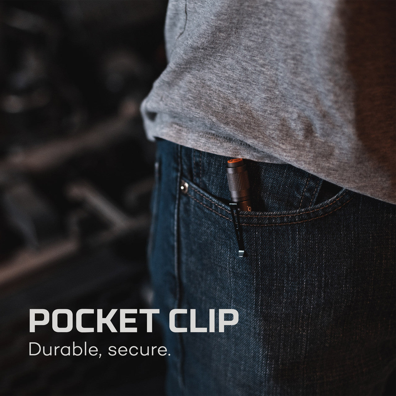 Pocket clip attached to a pair of jeans, partially visible beneath a gray shirt hem.