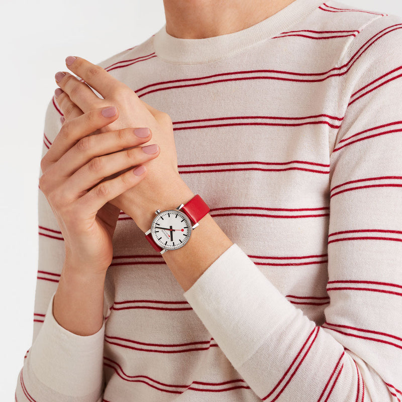Wristwatch with a red strap and white face on a person’s wrist.