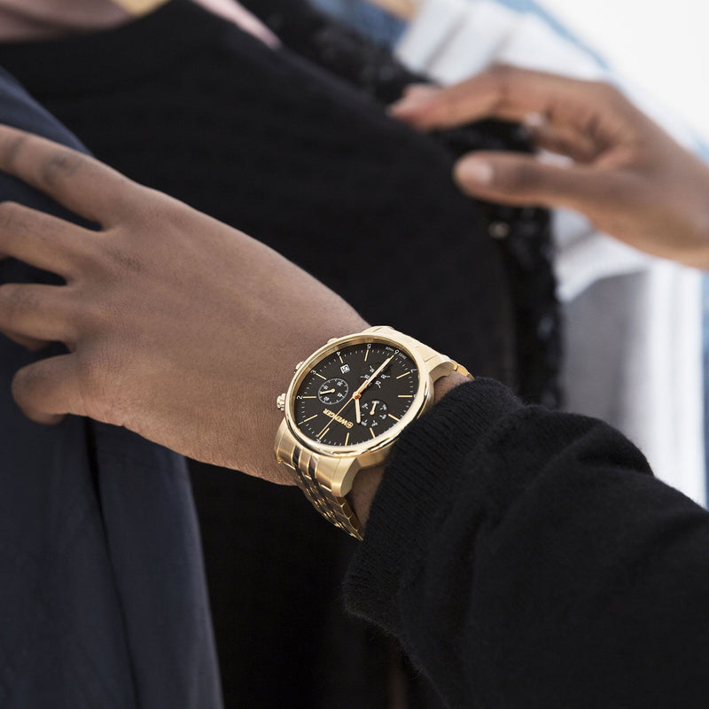 Gold wristwatch with a black dial and metal bracelet.