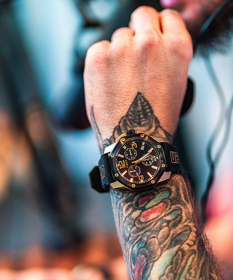 Wristwatch with a black and gold face worn over a colorful tattoo.