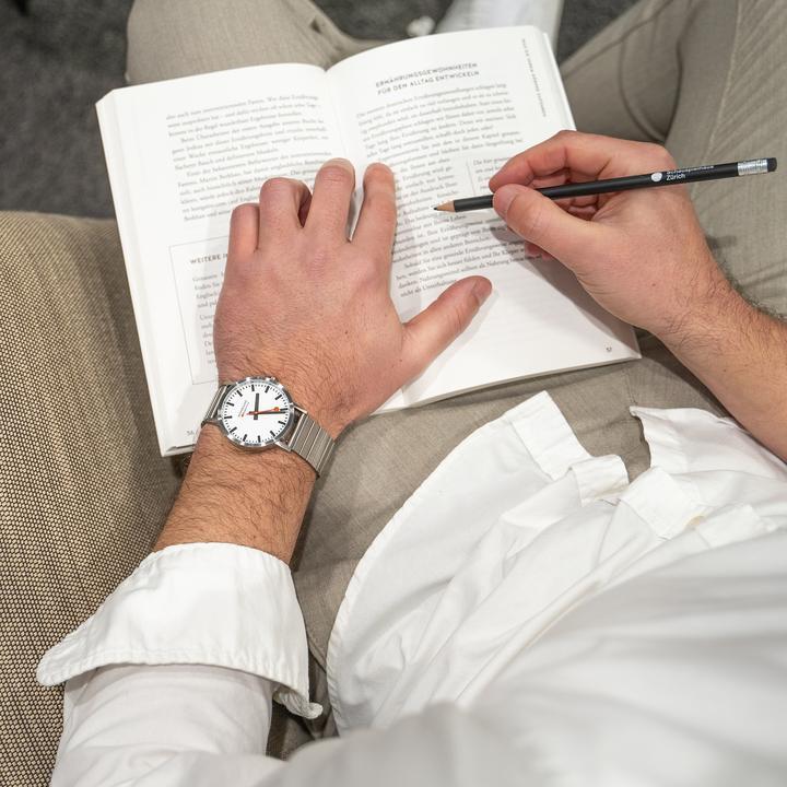 Open book with hands writing or taking notes, one hand wearing a wristwatch.