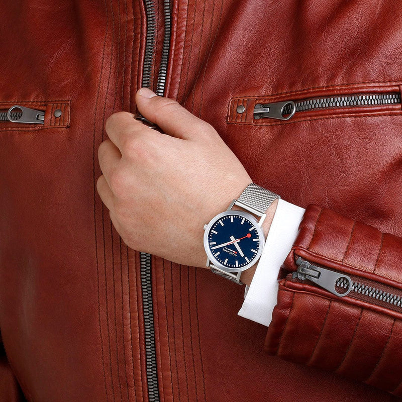 Wristwatch with a blue face and silver metal band on a person’s wrist.