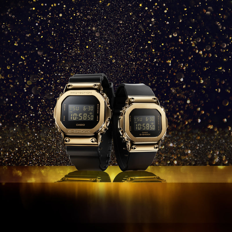 Two gold-toned digital watches with black straps displayed side by side.