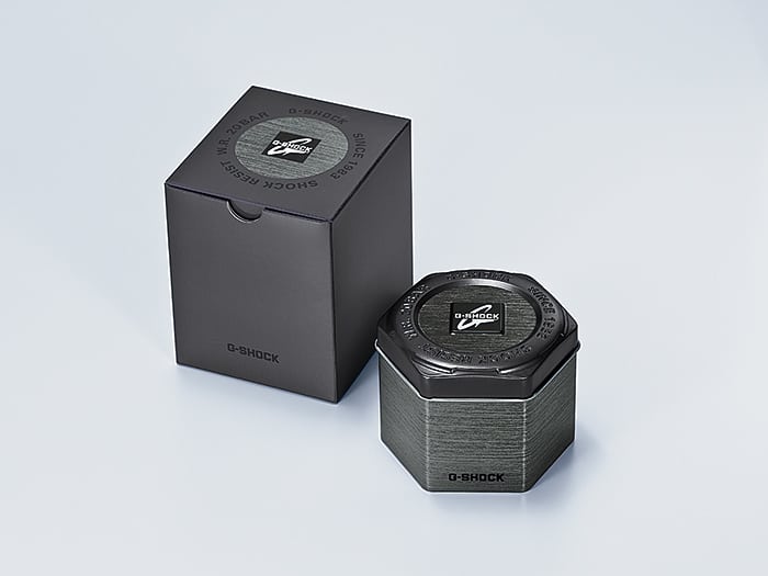 Hexagonal metallic watch box with a circular window on top.