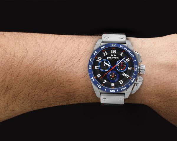 Wristwatch with a blue bezel and silver metal band worn on a person’s wrist.