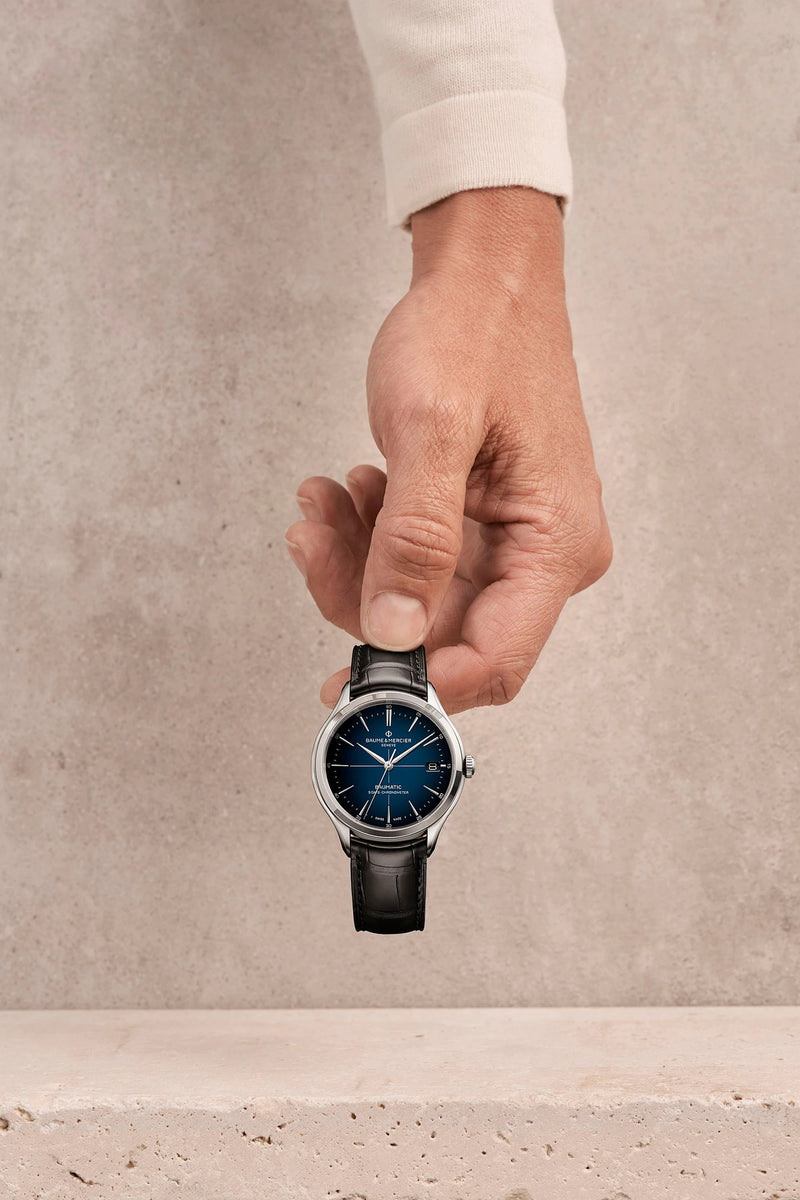 Wristwatch with a blue dial and black leather strap held by a hand.