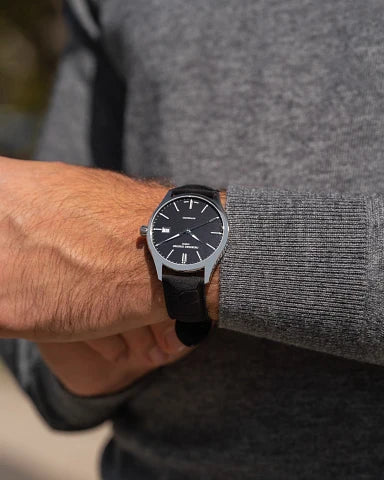 Wristwatch with a black face and leather strap worn on a person’s wrist.