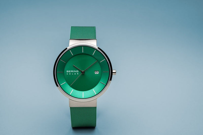 Green wristwatch with a round face and metallic mesh band.